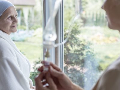 Sick senior looking at a nurse putting on a drip-bag in a hospital. Blurred photo