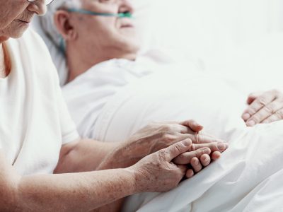 Senior man with lung cancer laying in hospice bed supporting by his elderly wife, photo with copy space